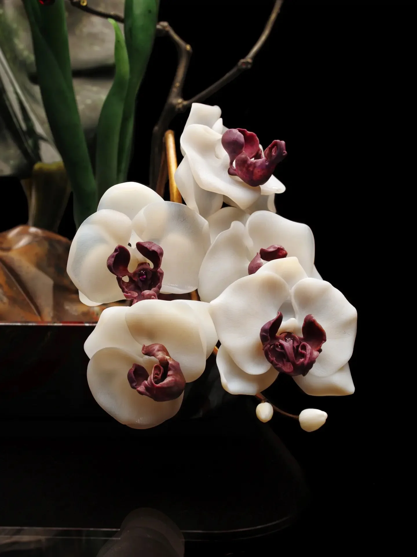 White orchid jewelry objects with sculpted burgundy centers, shown against a dark background.